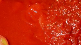 This closeup video shows fresh pasta sauce being stirred in pot with a spoon as it cooks.