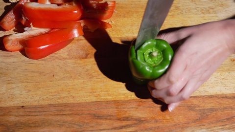 This POV video shows a top view of anonymous hands cutting a green bell pepper stem out on a wooden cutting board.