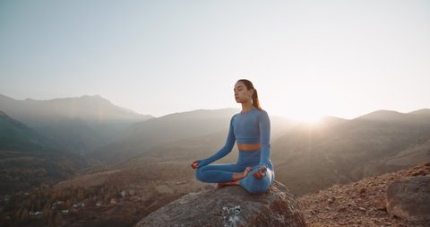 Fit girl doing lotus pose. Young athletic woman meditating in mountains, training and relaxing during sunrise - active lifestyle, zen concept 4k footage
