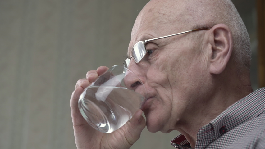 Bald elderly man with wrinkled face wearing glasses takes daily medication and drinks glass of water extreme close view | Shutterstock HD Video #1047525559