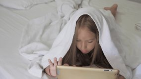 Teenage girl in bed playing a tablet in social internet. Close up of little girl watching video on the digital tablet.