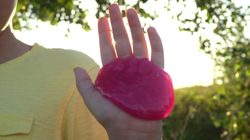 Closeup view of kids hand with sticky slime toy at sunny nature background.
