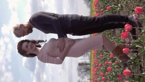 happy expectant family, young couple waiting of baby touching stomach and take pleasure vacation on flowers tulip lawn against clear sky, orientation 9:16