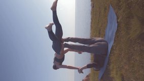 athletic couple practicing acro yoga on the mountain, female acrobat is balancing on the legs and hands of her male partner in sunlight on background of sky and the sea, orientation 9:16