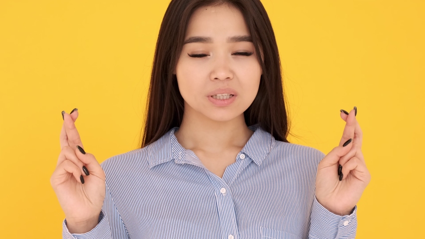 Young girl on a yellow background crossed fingers in hope that dreams come true