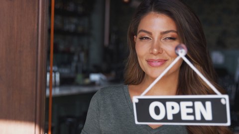 Female owner of coffee shop or restaurant walking up to door and turning round sign to open - shot in slow motion