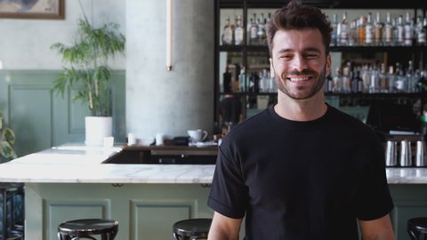 Portrait of male owner of restaurant bar standing by counter smiling and looking confident - shot in slow motion