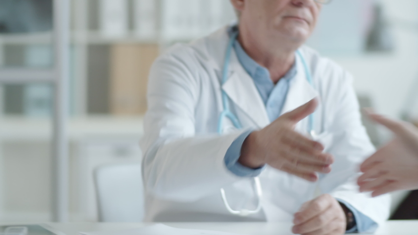 Midsection shot of mature doctor giving handshake and explaining something to male patient during medical consultation in clinic | Shutterstock HD Video #1047539812