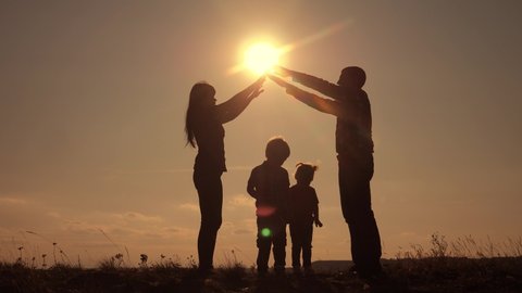 happy family teamwork silhouette shows a house and comfort symbol home at sunset. happy family mom dad and kids children portray a house roof hold their hands lifestyle over their heads home