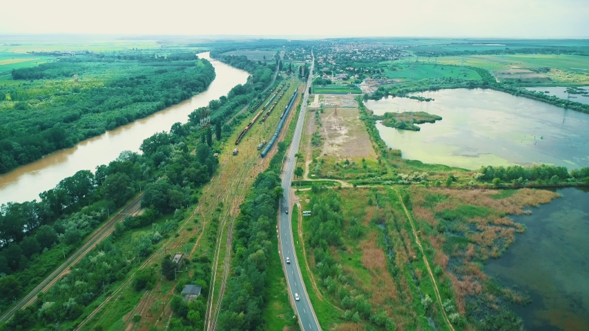 Bird-eye view on countryside landscape with highway traffic and railway tracks on the side.