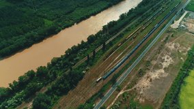 Top-view on many railway tracks and trains moving along a river in countryside.