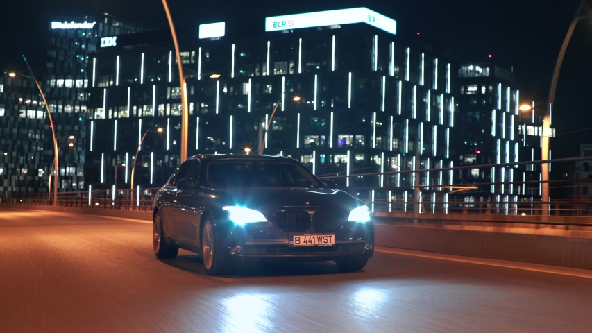 Bucharest, Romania - 02.20.2020: Crane rolling shot of a BMW 7 Series luxury sedan car driving on a city bridge at night with skyline view 
