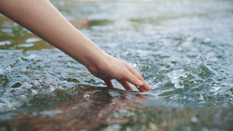 Hand touching water in the forest river or lake. People travel enjoying nature and life concept.