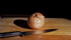 This closeup video shows anonymous hands cutting and peeling a fresh onion on a wooden cutting board.
