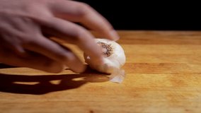This close up video shows anonymous female hands peeling garlic cloves on a wooden cutting board.