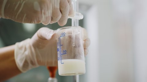 lab assistant in gloves adds reagent into beaker with testing milk in modern laboratory extreme close view