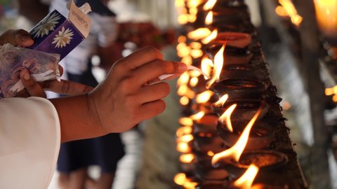 Closeup 4k footage of worshipper lighting up the wick of sacred oil lamp at buddhist temple