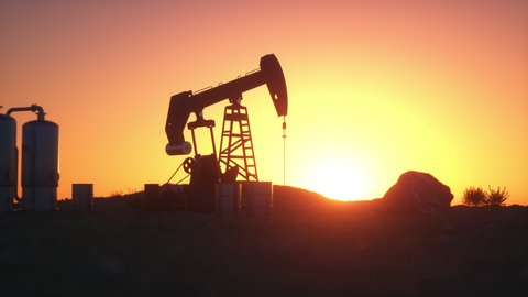 Oil pump jack in the desert as the sun sets, leaving its silhouette against the sky with refinery tanks, bushes and rocks. Loopable animation.