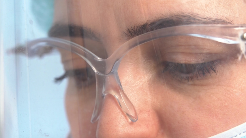 Very close-up of the doctor’s woman’s eyes through a transparent plastic protective mask and goggles during work | Shutterstock HD Video #1047582391