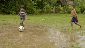 two young indigenous boys are playing football on a muddy pitch somewhere outside in their rural village general shot slow motion in ecuador - Powered by Shutterstock - Get 15% off with code: PIKWIZARD15