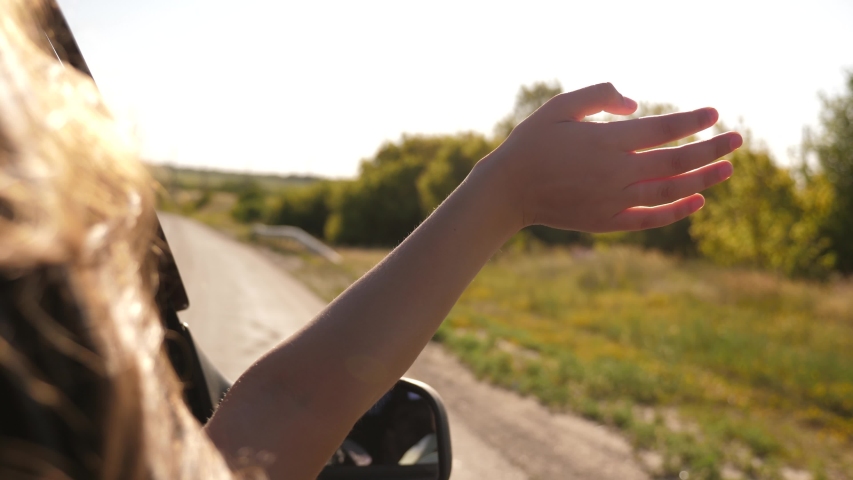 free woman travels by car catches the wind with her hand from car window. Girl with long hair is sitting in front seat of car, stretching her arm out window and catching glare of setting sun Royalty-Free Stock Footage #1047598105
