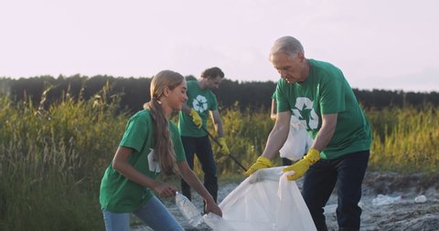 Caucasian grandfather holding bag and teen granddaughter picking trash and throwing in it while cleaning nature from pollution. Family of ecology activists. Environmental concept. Cute girl with man.