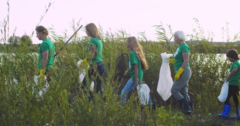 Whole Caucasian family with kids coming to lake shore with bags to clean nature on summer or spring day. Children with adults volunteering for keeping planet safe and ecological. Eco concept. Stock Video