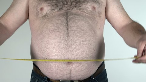 Adult fat man measures the circumference of his belly with tape measure. This footage is suitable to use in any project that has to do with obesity and healthy life. 