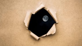 Creative 4k time laps video of a glowing full moon in the night sky with floating clouds, which is visible through a circle hole with torn edges in old retro grunge vintage paper.