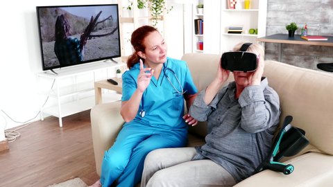 Female caregiver helping elderly woman to experience virtual reality to ease the pain in retirement home. Recovery treatment rehabilitation for patient. Elderly retired person in nursing home, caregiv