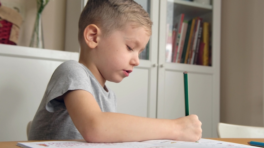 Preschool boy toddler, holding pencil, drawing or doing homework at the table. Close up