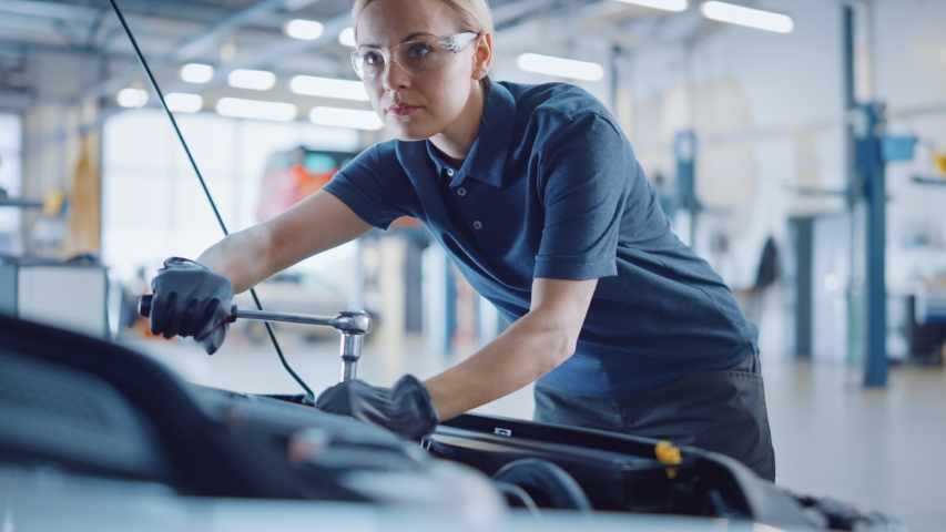 Beautiful Empowering Female Mechanic is Working on a Car in a Car Service. Woman in Safety Glasses is Working on an Usual Car Maintenance. She's Using a Ratchet. Modern Clean Workshop with Cars. | Shutterstock HD Video #1047624556