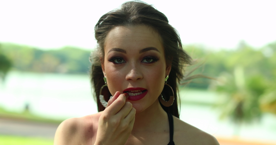 Woman applying red lipstick outside.
