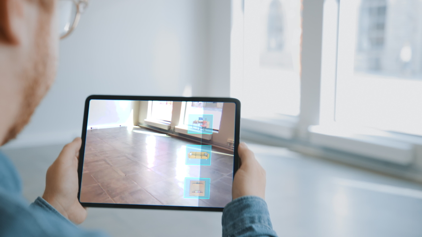 Decorating Apartment: Man Holding Digital Tablet with Augmented Reality Interior Design Software Chooses 3D Furniture for Home. Man Pick Sofa, Table and Lighting for Living Room. Over Shoulder Screen  Royalty-Free Stock Footage #1047633148
