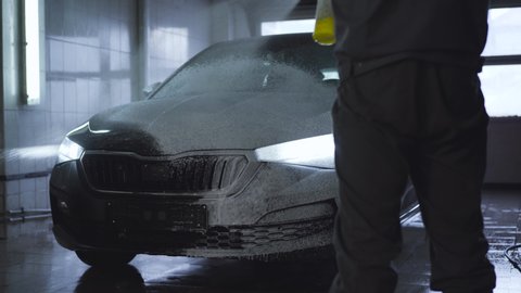 Worker spraying car with pressure washer in auto care shop. Employee washing automobile with special product. Service maintenance, business, industry.