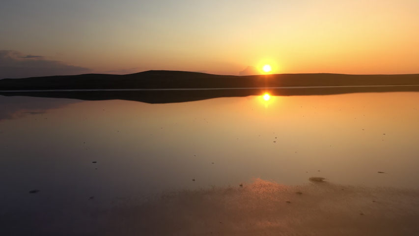 Flying over Kayashsky lake to the side against the background of a bright and beautiful sunset. Aerial shot of lake in Crimea, Ukraine, top view, in slow motion. The sun is reflected in the water.