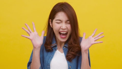 Portrait of young Asian lady with positive expression, excited screaming, dressed in casual clothing and looking at the camera over yellow background. Happy adorable glad woman rejoices success.