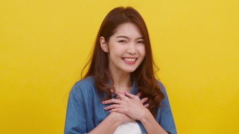 Portrait young Asian lady with positive expression, joyful and exciting, dressed in casual cloth and looking at camera over yellow background. Happy adorable glad woman rejoices success. Slow motion.