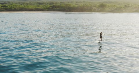 Aerial view of a man on an electric hydrofoil personal water craft surfboard riding in the ocean at sunrise, the future of water vehicles and transport Video Stok