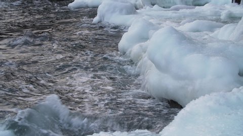 Cold sea waves crashing at shore covered with ice and icicles. Winter