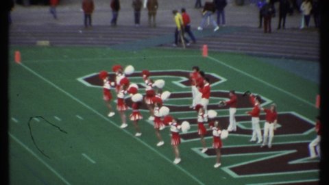 ITHACA NEW YORK-1979: Girl Cheerleaders Wave Pom Poms In Front Of Boy Cheerleaders Then Marching Band Forms An Anchor