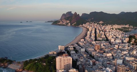 Flying along Ipanema Beach overlooking beautiful morning light on buildings by the ocean. Wide angle panorama of Rio de Janeiro, Brazil and Mountains on the horizon