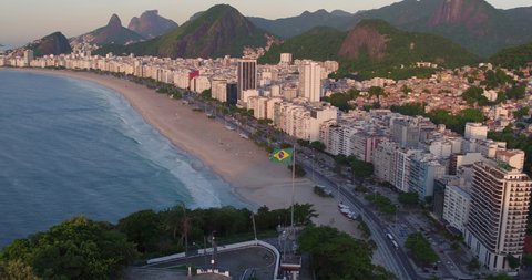 Aerial panorama of Copacabana Beach at sunrise in Rio de Janeiro. Dynamic shot with Brazilian flag waiving on the top of the hill as foreground