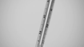 Closeup view black and white video of glass thermometer with raising line of high human body temperature isolated on light grey background.