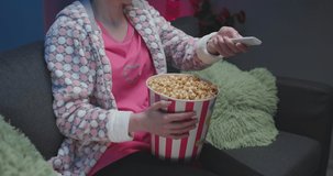 Woman watching funny movie on the tv and eating popcorn on sofa