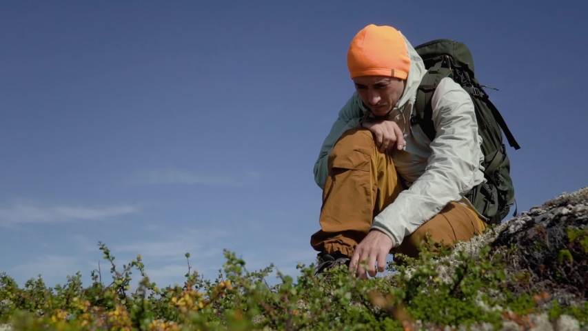 A hiker touches the grass with his hand. He is in the tundra.