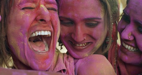 Close-up CU multiethnic group of 4 friendly women hugging posing faces next to each other coloured red, green, yellow, pink, gulal laal celebrating festival of Holi, India- slow motion handheld 60 fps