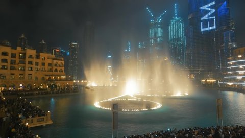 Dubai, UAE - February 2020 : Musical and dancing fountain with lighting in Dubai city at night, UAE. View from balcony at show, skyscrapers and many tourists