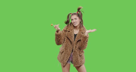 Fashion girl wearing leopard fur coat licking candy. Freak young sexy woman with lollipop having fun . Vogue style female dancing over green screen background chroma key