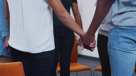 Multi-cultural group of men and women joining hands at mental health group therapy meeting - shot in slow motion
